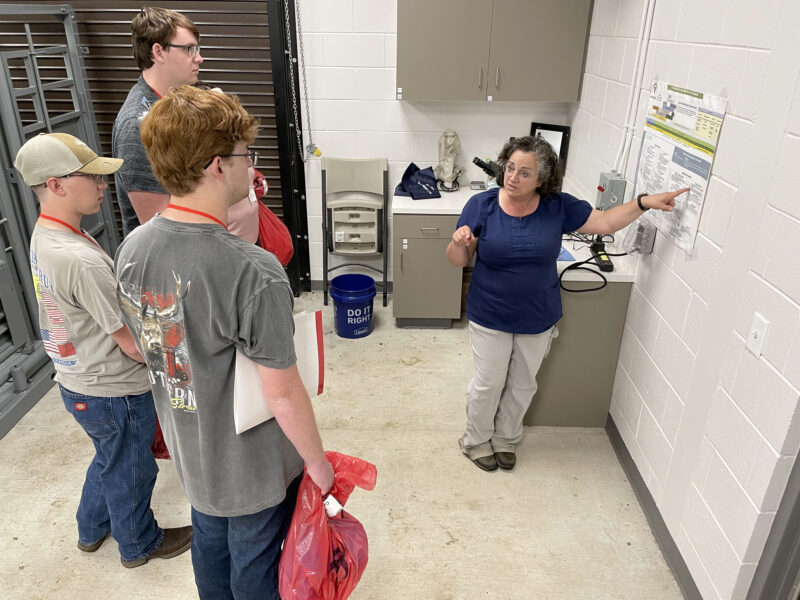 a group of students watching Angie McDaniel as she shows them her work space.