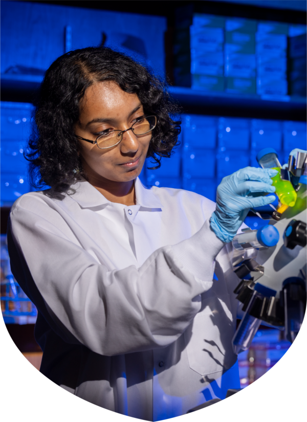 a woman wearing a white coat and glove places a test tube into a piece of lab equipment