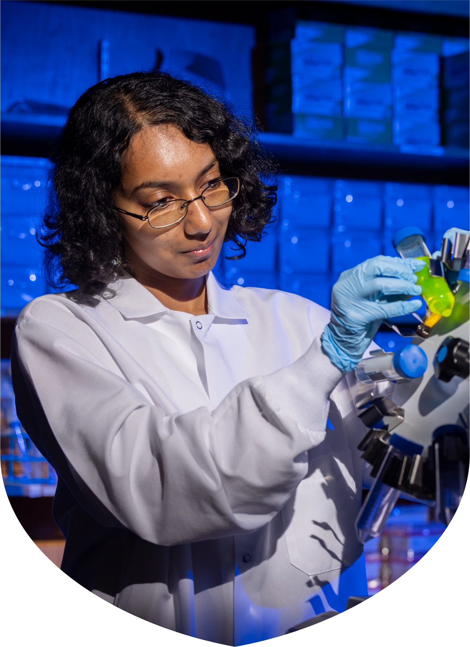 a woman wearing a white coat and glove places a test tube into a piece of lab equipment